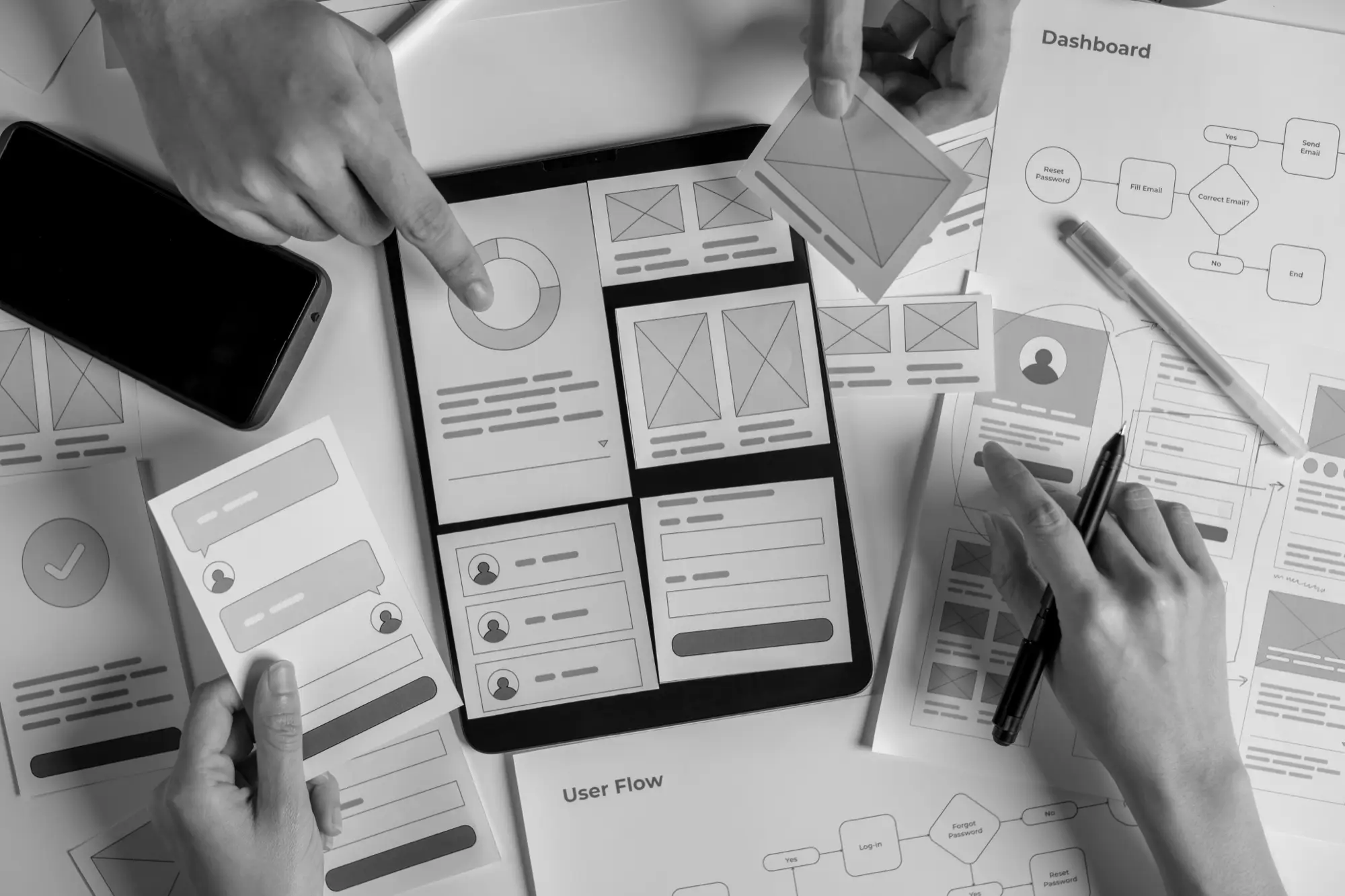 Wireframes, user-flow diagrams, and a tablet prototype spread across the design table